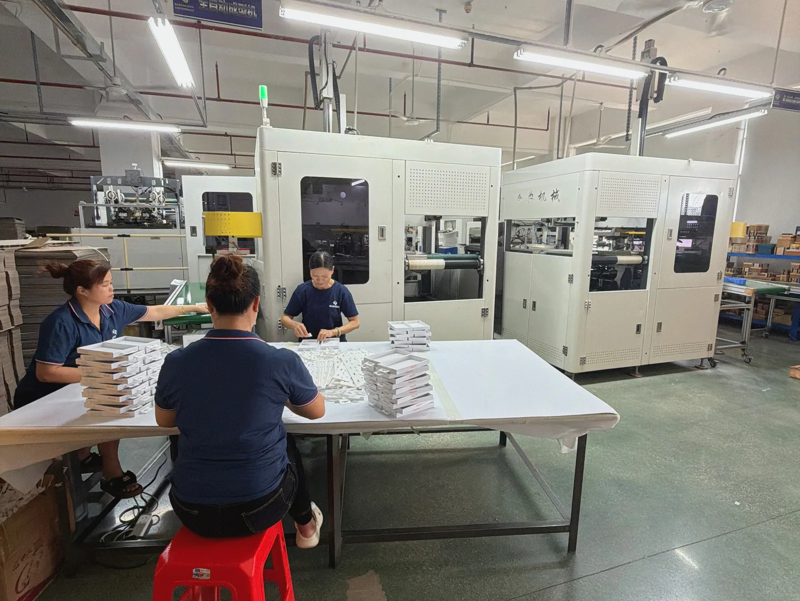 Staff sorting and assembling small paper packages beside production equipment
