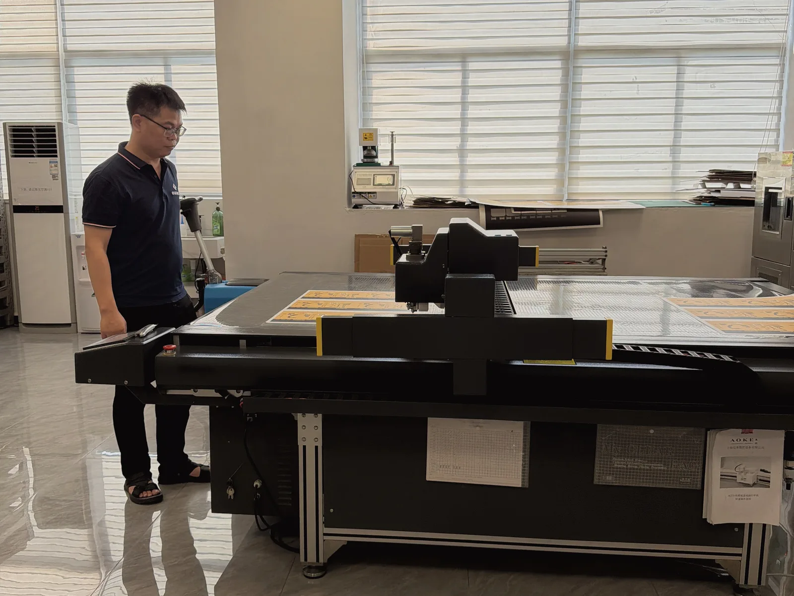 Operator beside a digital sample-cutting workstation in a packaging factory